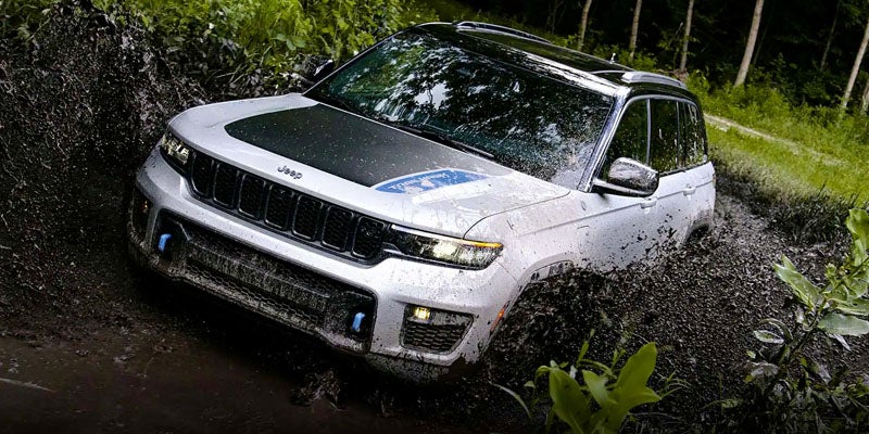 White Jeep Grand Cherokee 4xe off-roading through deep mud in a forest