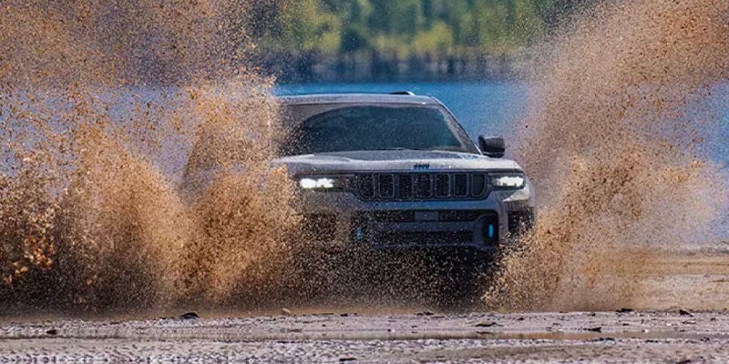 2025 Jeep Grand Cherokee splashing through mud near a lake