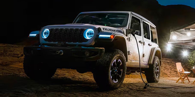 Jeep Wrangler 4xe charging at night near a campsite