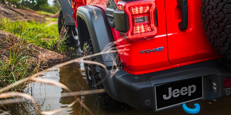 Rear view of red Jeep Wrangler 4xe driving through water on an off-road trail