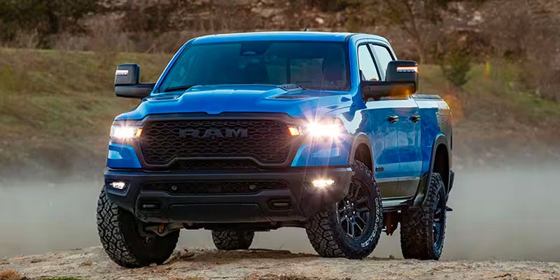 Blue RAM 1500 parked on a rugged mountain road with scenic mountains in the background.