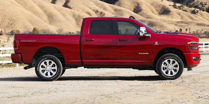 A red Ram 2500 pickup truck is parked on a dirt road in a dry, hilly landscape.